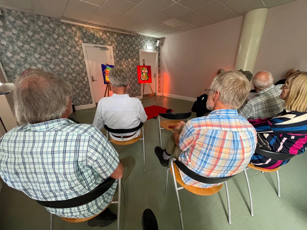 Publikum sidder og ser på malerier på staffelier